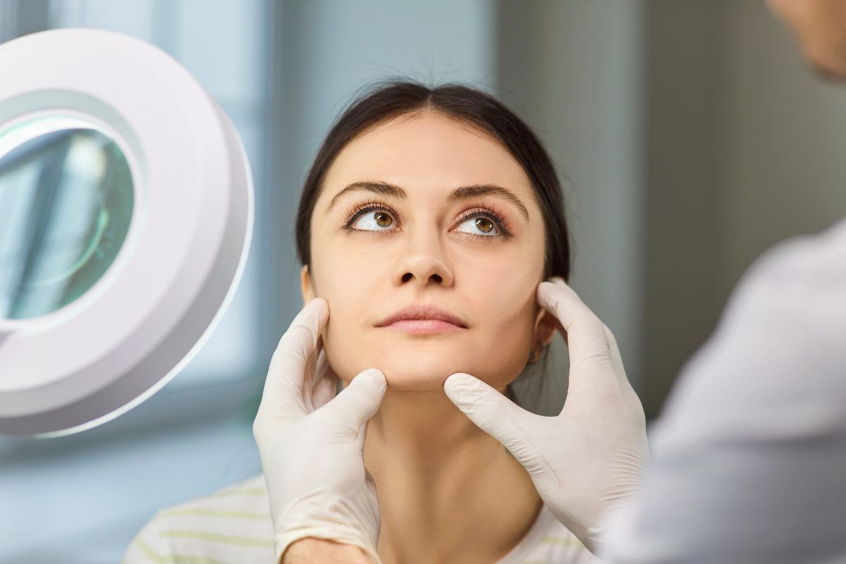 Esthetician examining a client’s skin beside a magnifying lamp
